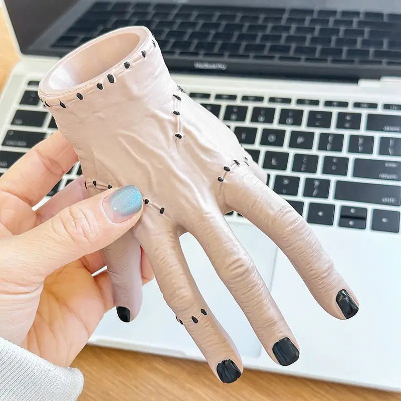 A hand holds a light pink resin Halloween hand planter and pen holder against a white laptop background.