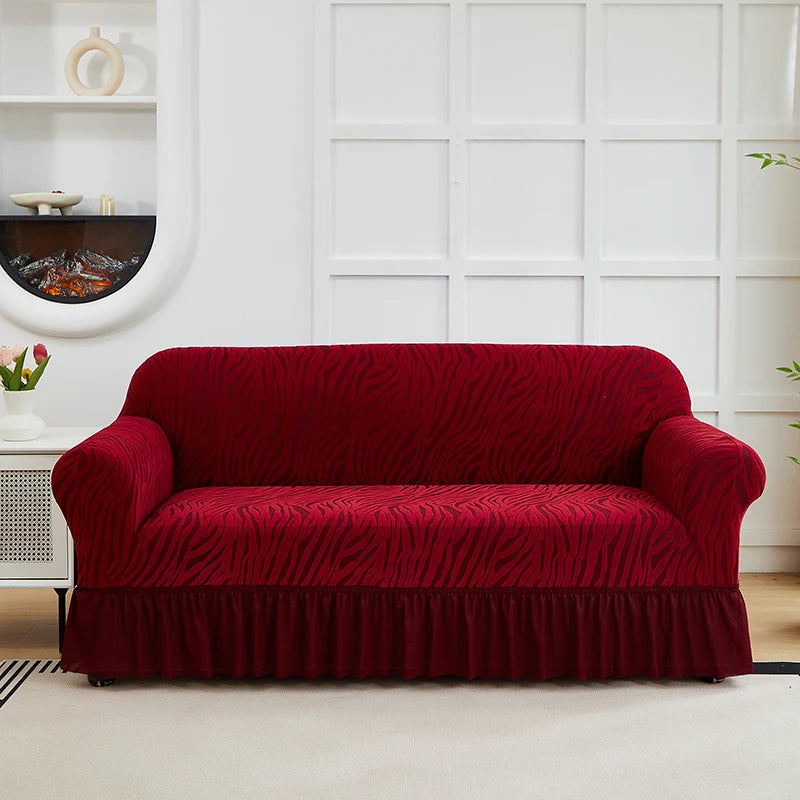 A deep red jacquard sofa cover with an elastic skirt displayed on a white sofa against a light wall.