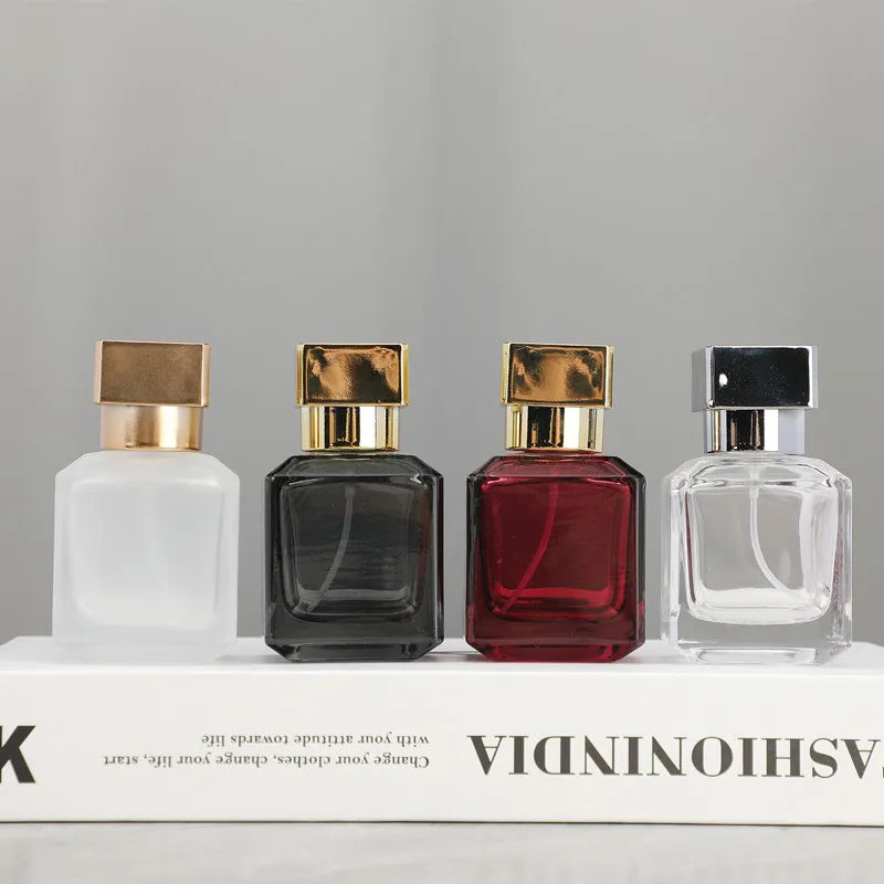 Four glass perfume bottles of varying colors and shapes displayed on a white box.