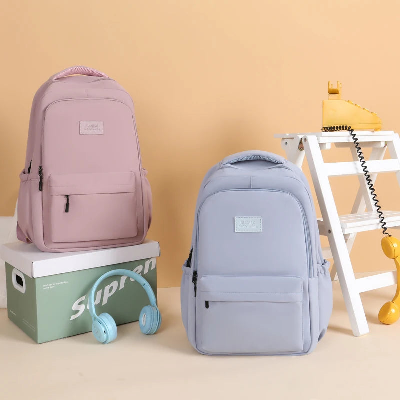 A pink and light blue waterproof nylon laptop backpack displayed on a white wooden shelf.