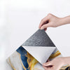 Hands are peeling a piece of marble-patterned peel-and-stick wall tiles from a sheet.