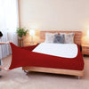 A red stretch-fit box spring cover is displayed on a wooden bed frame with fluffy pillows.