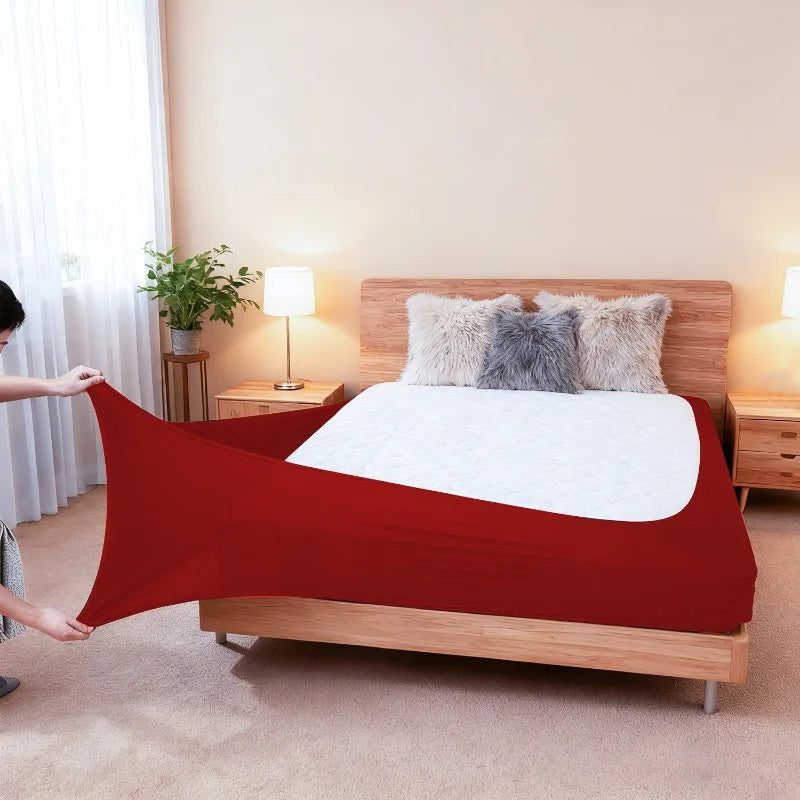 A red stretch-fit box spring cover is displayed on a wooden bed frame with fluffy pillows.
