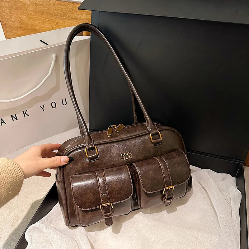 Braune Umhängetasche mit Goldhardware liegt auf einem weißen Stoff.