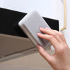 A hand is holding a gray double-sided cleaning sponge against a black cabinet surface.