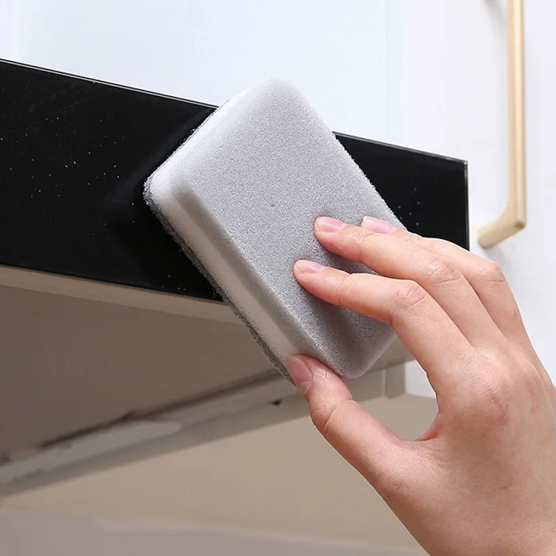 A hand is holding a gray double-sided cleaning sponge against a black cabinet surface.