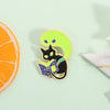 A set of enamel pins featuring a cat reading a book on a lime green background.