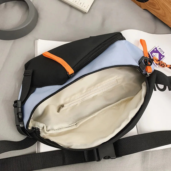 A black and light blue utility chest bag with an orange strap and a zippered interior pocket resting on a white notebook.