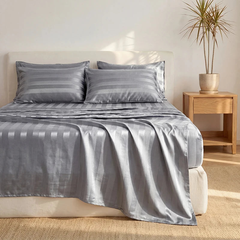 A gray striped satin bedding set featuring a duvet cover and pillows on a bed.
