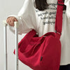 A person holds a large red canvas travel tote bag with a crossbody strap in front of a white shirt.