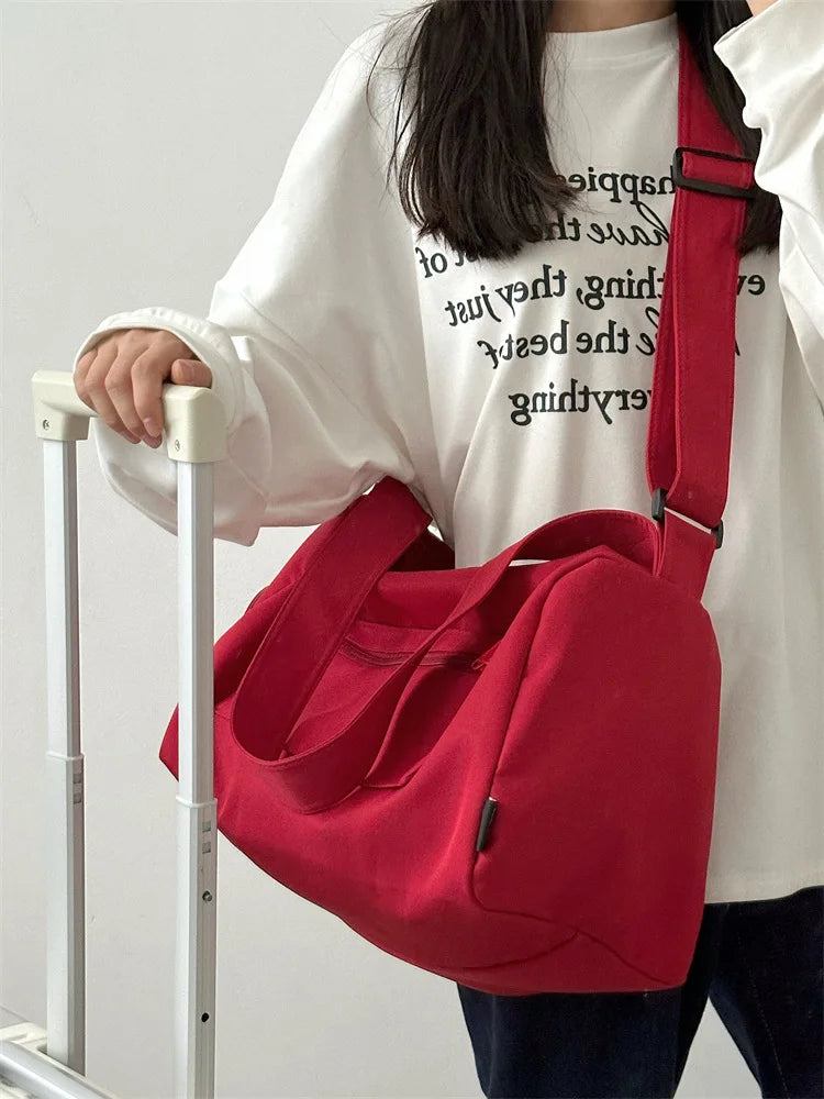 A person holds a large red canvas travel tote bag with a crossbody strap in front of a white shirt.