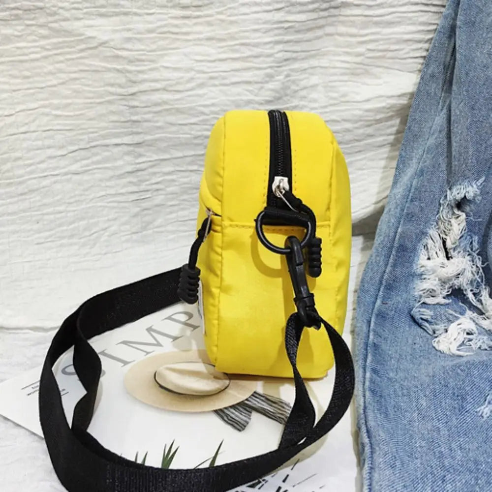 A yellow mini canvas crossbody bag with a black strap is shown against a white background.