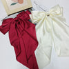 A pair of silk bow hair clips in deep red and cream colors displayed next to a card.
