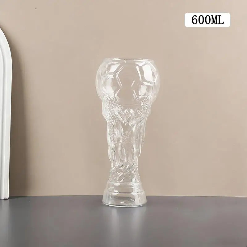 Klares Glaspokal in Form eines Fußballs, Bierbecher auf grauer Oberfläche.