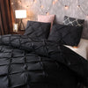 Black quilted comforter and pillows on a bed with a gray wall and string lights.