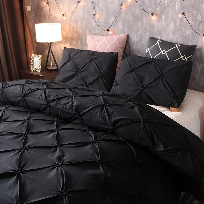 Black quilted comforter and pillows on a bed with a gray wall and string lights.