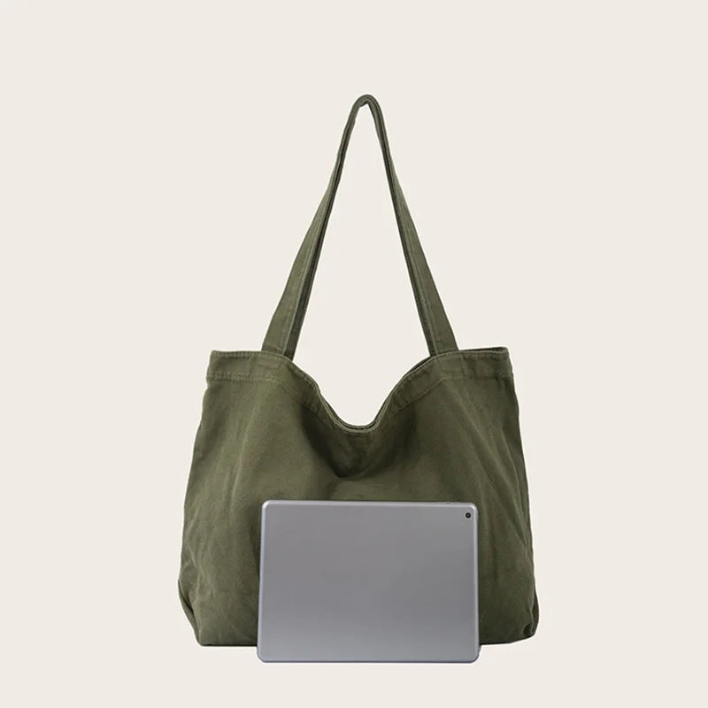 Sac cabas en toile vert olive foncé avec longues anses, posé à côté d'une tablette argentée.
