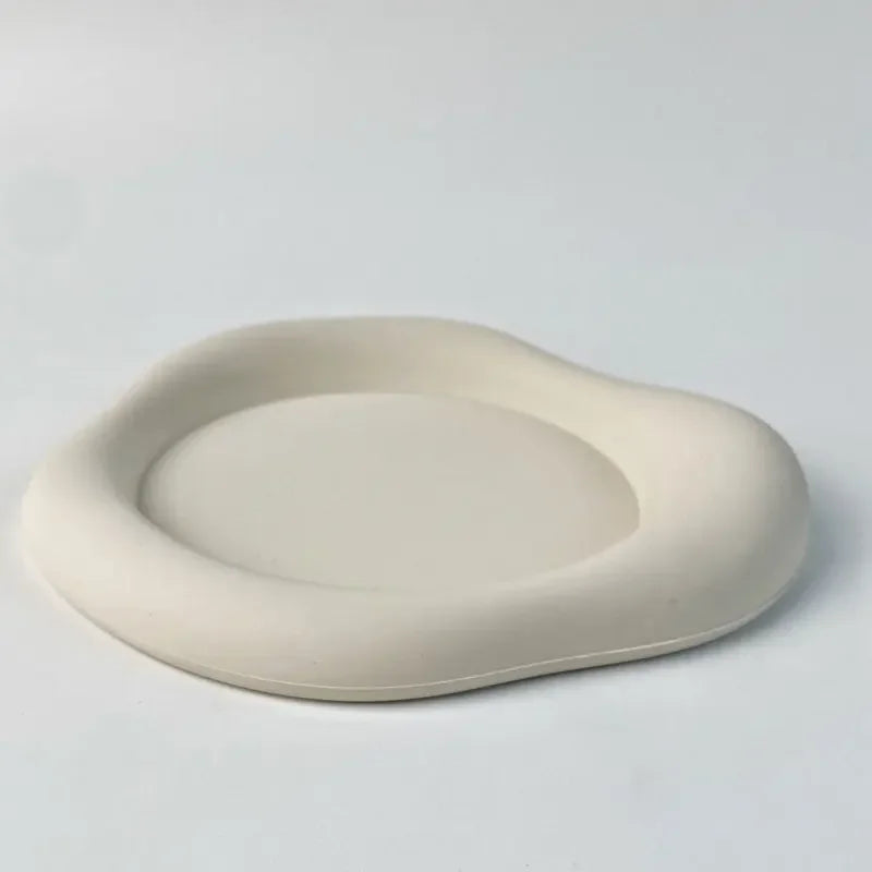 A round, light beige silicone coaster with a slightly raised rim is shown on a white surface.