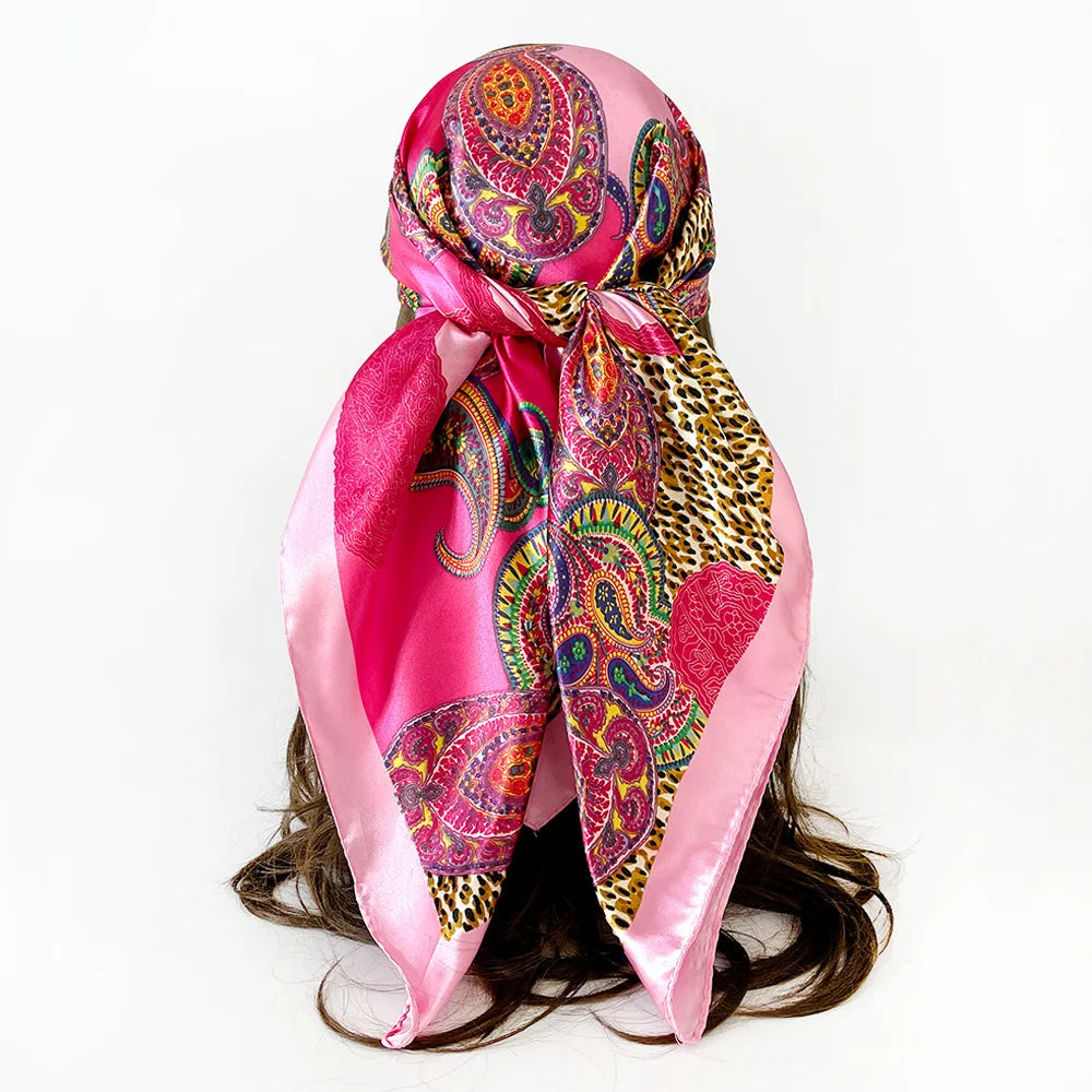 A vibrant pink leopard and paisley square scarf tied around a dark hairstyle.
