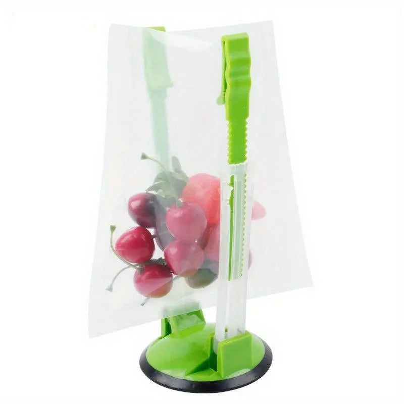 A clear plastic bag holder rack with green handles is shown holding several pink and red apples.