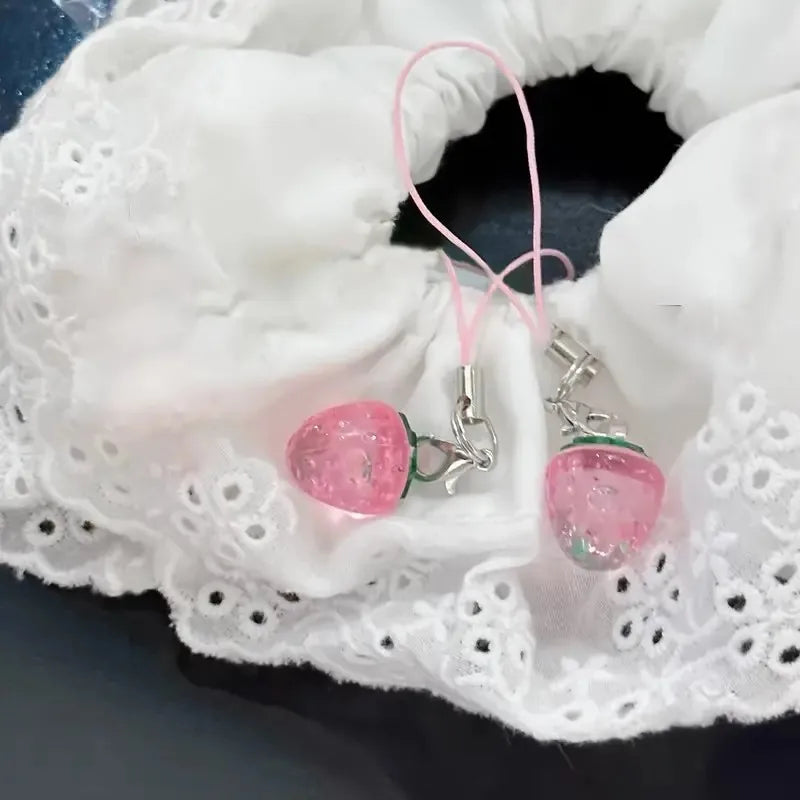 Pink strawberry resin phone charm keychain attached to white lace fabric