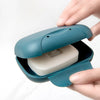 A hand opens a teal leak-proof travel soap box revealing a white bar of soap.