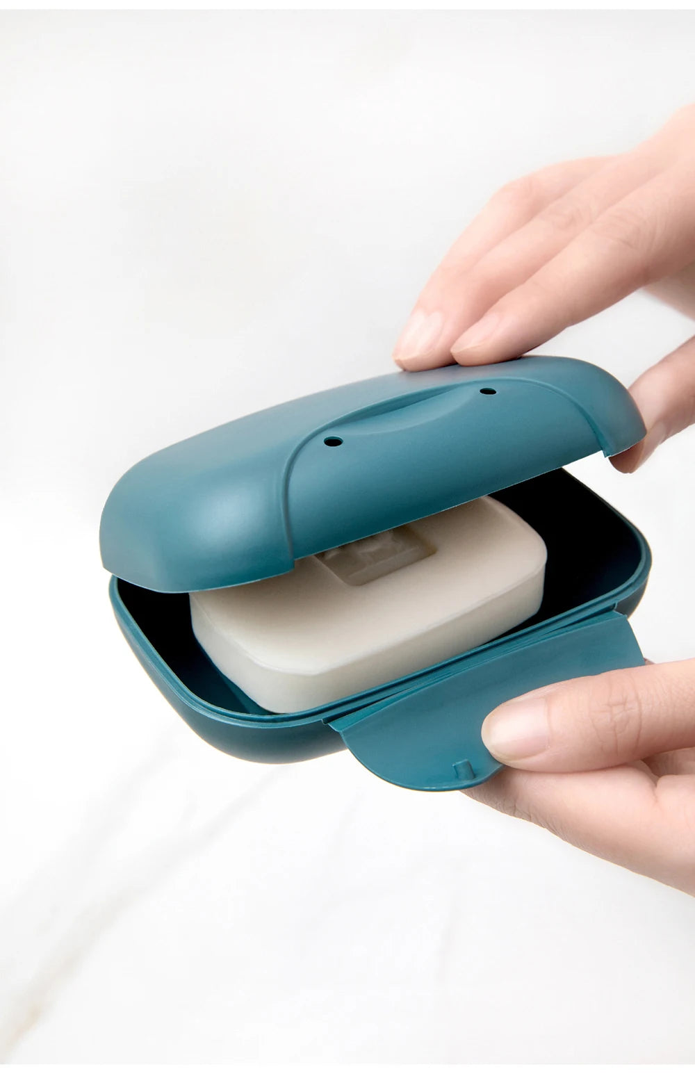 A hand opens a teal leak-proof travel soap box revealing a white bar of soap.