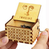 A wooden music box with a lid featuring an eye design and the word IMAGINE is held in a hand.