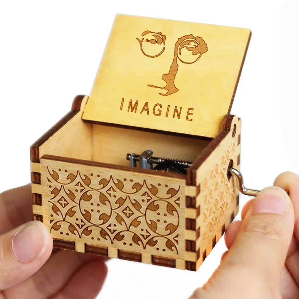 A wooden music box with a lid featuring an eye design and the word IMAGINE is held in a hand.