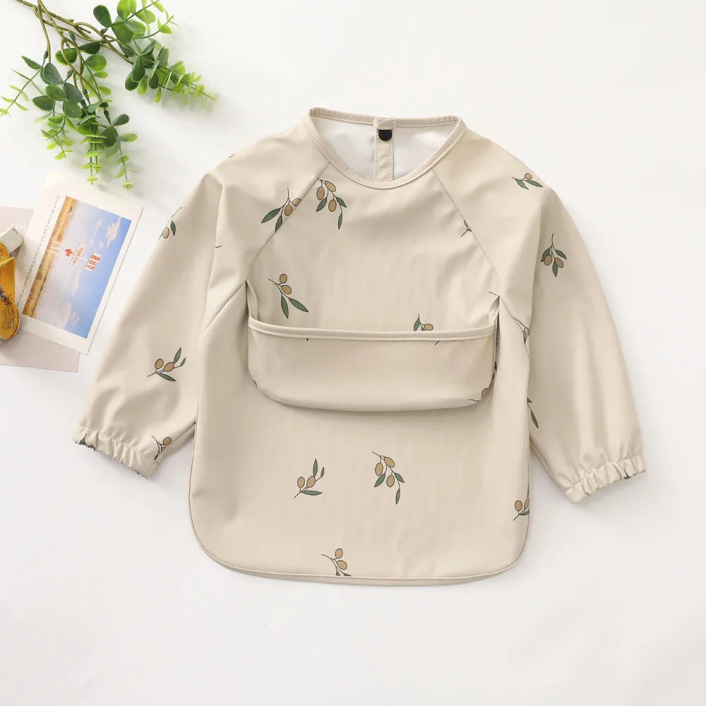 A beige waterproof long-sleeve smock for toddlers with a subtle olive leaf pattern.