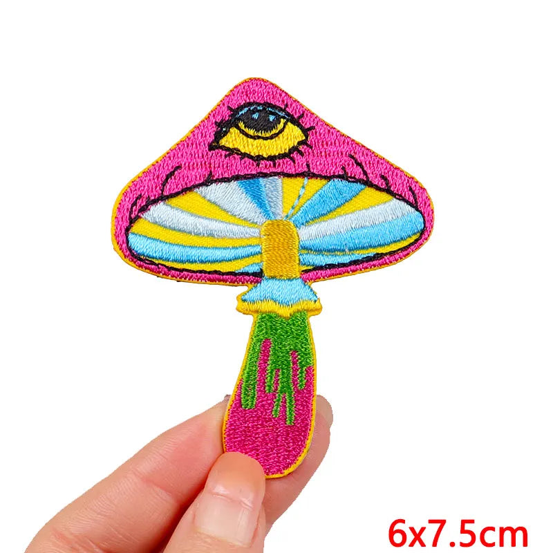 A vibrant pink and yellow embroidery patch depicting an eye with a striped iris, shown being held by a hand.
