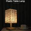 A poetic table lamp with a rectangular linen shade and wooden base, illuminated to display calligraphy.