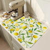 A yellow and green lemon print absorbent kitchen drying mat placed on a light-colored cabinet surface.