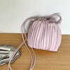 A pale pink pleated faux leather crossbody bag with a matching strap resting on a wooden surface.
