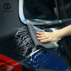 A hand is using a gray detailing towel to wipe white clay residue off a dark blue car paint surface.