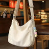 A cream-colored canvas bag with a strap and a decorative keychain featuring colorful macaron-shaped charms.