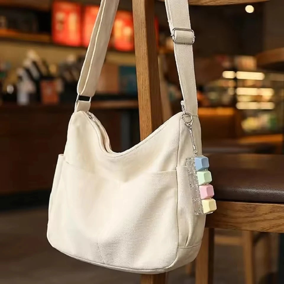 A cream-colored canvas bag with a strap and a decorative keychain featuring colorful macaron-shaped charms.