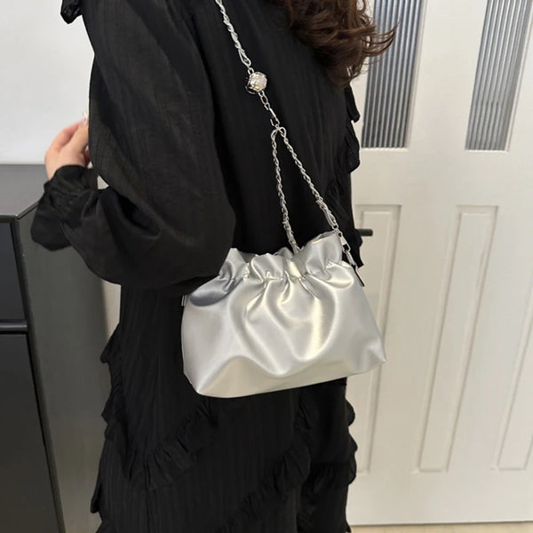 Eine Frau hält eine silberne Satin-Bucket-Crossbody-Tasche gegen ein schwarzes Rüschen-Oberteil.
