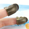 A vintage metal sewing thimble shaped like a finger protector ring worn on a person's finger.