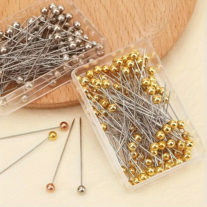 A clear plastic container holds a pack of precision quilting pins in silver and gold colors.