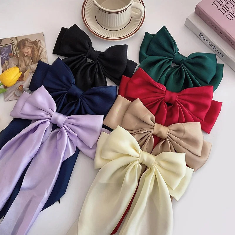 A collection of silk bow hair clips in various shades including black, navy blue, purple, and olive green.