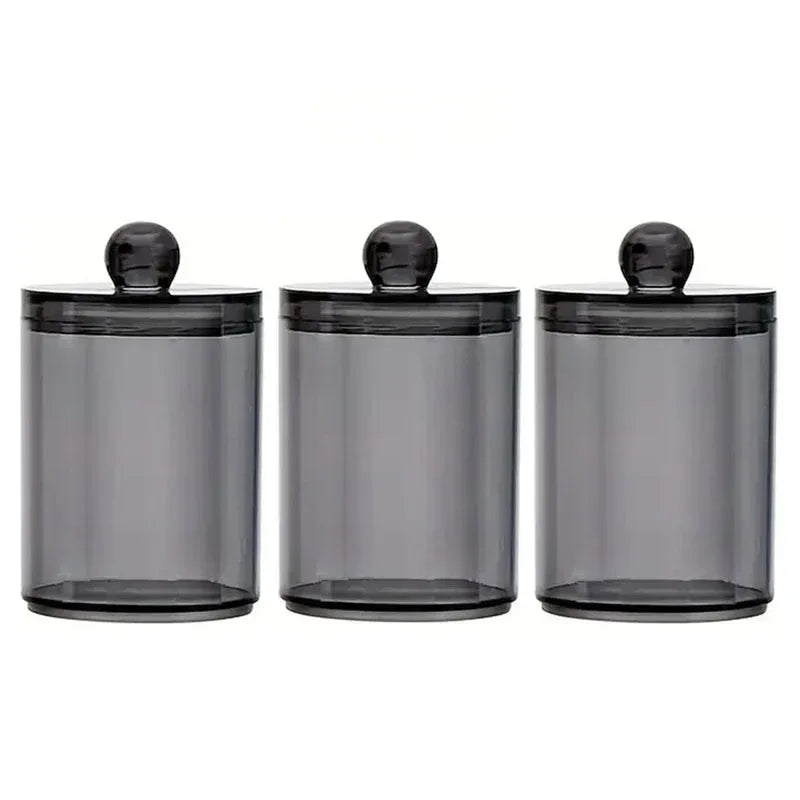 A set of three clear glass apothecary jars with black lids for storage and organization.