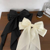 A black silk bow hair clip and a cream colored silk bow hair clip are displayed on a wooden surface.
