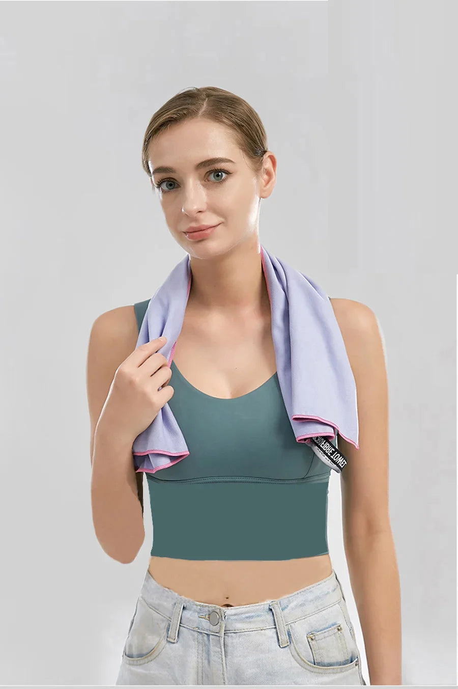 A woman models a purple microfiber sports towel top and light blue jeans against a gray background.