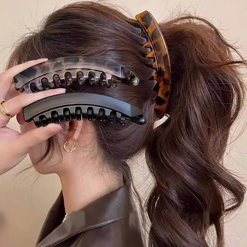 A hand is shown placing a black hair clip with an tortoiseshell pattern into a woman's dark brown hair.