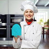 A smiling woman wearing a white chef coat and hat holding a blue silicone oven mitt.