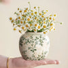 Eine Hand hält eine weiße Keramikvase, gefüllt mit gelben und weißen Margeriten.