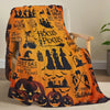 An orange Halloween themed flannel throw blanket featuring carved pumpkins and witches on a wooden chair.