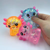 A hand holds a translucent squishy stress ball shaped like an axolotl in various colors.