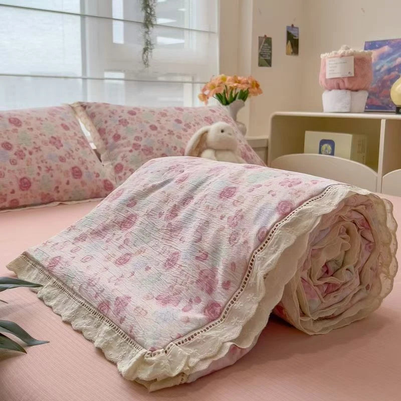 A pink floral washed cotton gauze summer quilt rolled up on a bed.